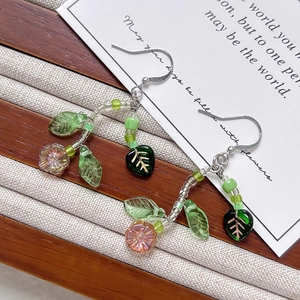 Handmade daisy earrings with pink glass flowers and green leaves on wood surface