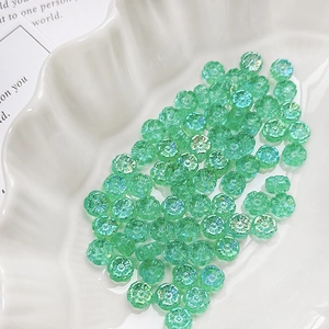 Macro view of iridescent green daisy glass beads in a white shell-shaped dish