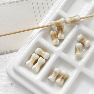 Macro detail of bone-shaped ceramic beads for DIY jewelry making on a white tray