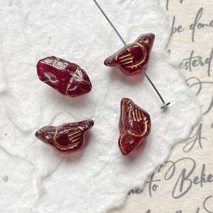 Macro detail of bird-shaped deep red glass beads with gold textured engravings