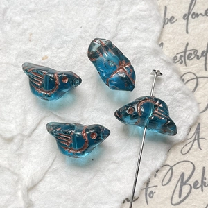 Macro shot of blue bird-shaped beads for DIY jewelry making with antique bronze detail