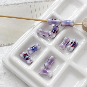 Detailed view of lavender bone-shaped ceramic beads with floral patterns in a white tray
