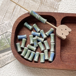 Detailed macro shot of bamboo-shaped ceramic beads with light green glaze in a wooden tray