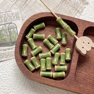 Detail of green bamboo-shaped ceramic beads with speckled glaze on a rustic wooden tray