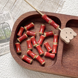 Detail of red glazed ceramic bamboo beads with dark spots on wooden tray for DIY jewelry