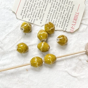 Vista dettagliata di perle in ceramica smaltata giallo senape con trama maculata e bastoncino