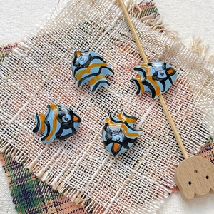 Macro view of four hand-painted ceramic tropical fish beads for DIY jewelry making
