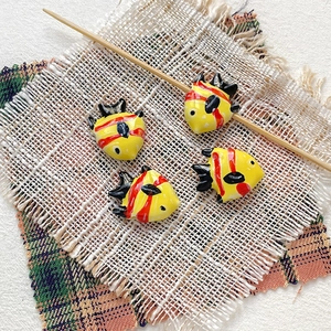 Close-up of four handmade yellow ceramic tropical fish beads with red stripes for DIY jewelry