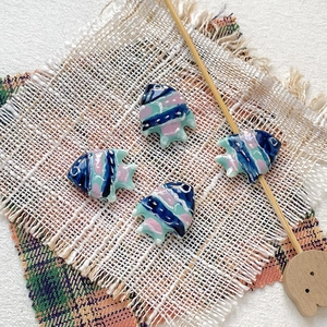 Detailed view of hand-painted ceramic tropical fish beads for DIY jewelry on linen