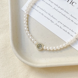 Retro gold-plated pearl necklace with a sea blue zircon pendant on a textured beige tray