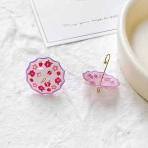 Close-up of purple resin umbrella earrings with floral and strawberry print on white texture