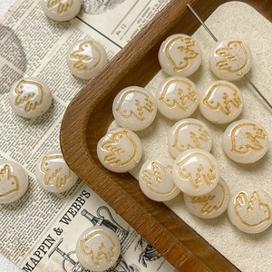 Macro shot of cream white round beads with golden bird engraving for DIY jewelry