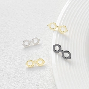 Detail of mini gold-plated spectacles shaped metal accessories in three metallic finishes