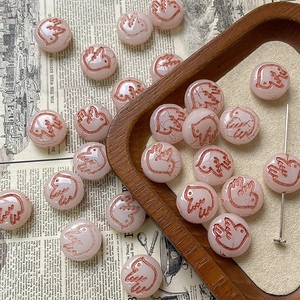 Macro detail of hand-painted pink glass beads featuring bird engravings for DIY jewelry making