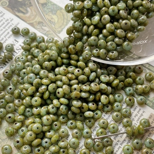 Macro detail of olive green Czech glass beads with vintage texture spilling from a glass