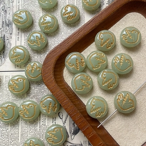 Macro detail of round light green Czech glass beads with golden hand-painted bird design