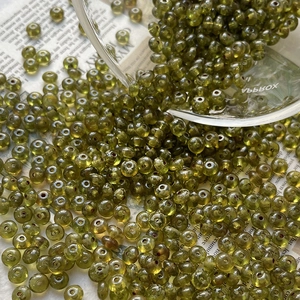 Macro view of olive green translucent glass seed beads scattered on vintage newspaper