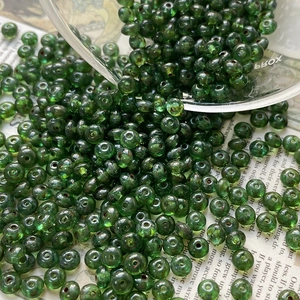 Macro shot of transparent dark green Czech glass beads pouring from a glass bowl