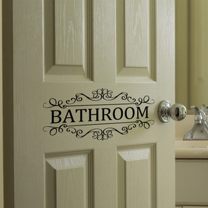 Classic black vinyl bathroom door decal with elegant ornate scroll frames on a wooden door