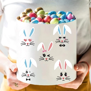 Boîte cadeau de Pâques avec visages de lapins en mains, remplie d'œufs en chocolat