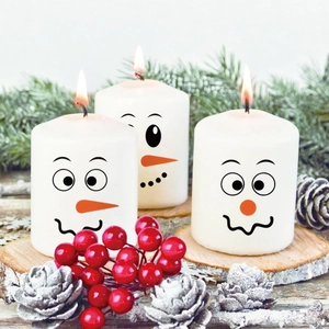 Close-up of three festive snowman face candles set on a wooden tray with pine decorations