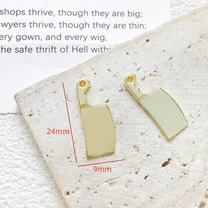 Detailweergave van twee gouden hakmes-bedels voor DIY-sieraden op een stenen ondergrond