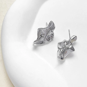 Detailansicht der 14k vergoldeten Ohrstecker im unregelmäßigen Lavadesign auf Keramikschale