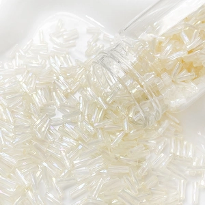 Detailed macro view of 6mm cream iridescent bugle beads pouring from a glass jar