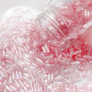 Macro shot of iridescent pink bugle beads spilling from glass bottle on white surface