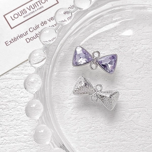 Detalle de dijes de lazo plateados con cristales morados para joyería artesanal DIY