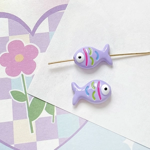 Macro detail of two purple hand-painted fish beads on a gold wire for DIY jewelry making