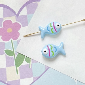 Detailed macro view of two light blue ceramic fish beads with colorful hand-painted scales
