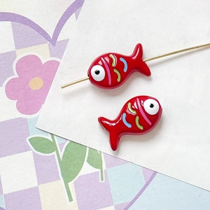 Close-up of hand-painted red ceramic fish bead on a golden pin for DIY jewelry making