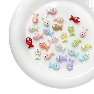 Colorful hand-painted fish beads for DIY jewelry making on a white ceramic plate