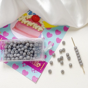 Macro detail of 4mm frosted grey glass beads with storage box and beading needle tool