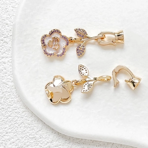 Macro detail of 18k gold plated camellia flower connector with zircon and white enamel