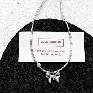 Silver bead necklace featuring a pearl accent and polished metal bow pendant on felt