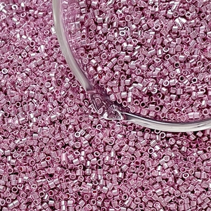 Macro shot of pink metallic cylindrical glass seed beads in a transparent glass container