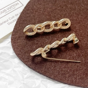 Detail of twisted cable and chain link gold-plated safety pin brooches on felt
