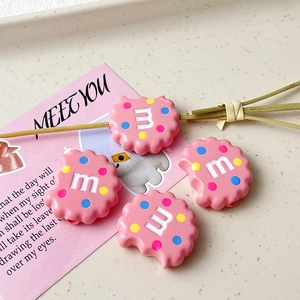 Detail von rosa Harzanhängern in Keksform mit M-Buchstaben und bunten Punkten für DIY