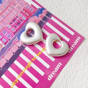 Dettaglio di ciondoli a cuore finitura perlata con centro vuoto su rivista rosa