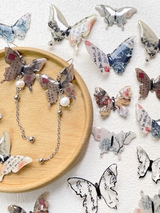 Detail of long butterfly drop earring with calligraphy pattern and white pearl charm