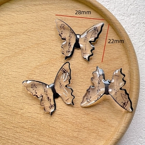 Close-up of butterfly pendants with vintage calligraphy and size details on wood tray