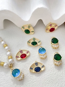 Detail view of gold-plated evil eye charms with colorful zircon inlay on white sand