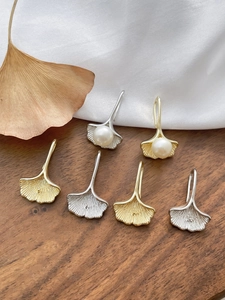Detailed view of 14k gold-plated ginkgo leaf ear hooks with pearls on wood surface