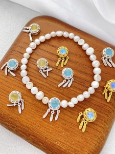 Close-up of pearl bracelet with dreamcatcher charm and feather pendants on wood base