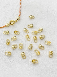 Macro shot of 14k gold-plated bead tips for jewelry finishing on a textured white background