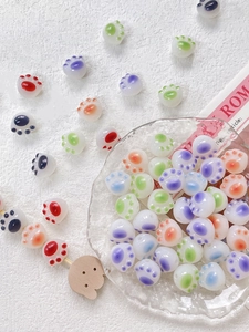 Colorful resin cat paw beads scattered on a glass tray for DIY jewelry making