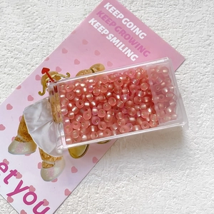 Close-up of 3mm pink cat-eye glass beads in a transparent plastic storage box