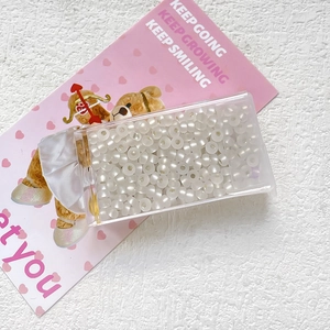 Close-up of 3mm cream cat eye glass beads for DIY jewelry making in a plastic box